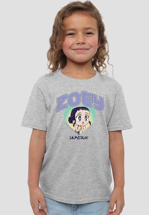Lächelndes junges Mädchen mit lockigem Haar, das ein graues T-Shirt trägt, das einen Cartoon-Charakter und die Texte "ZOEY" und "HUNTRAX" zeigt.
