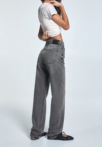 Jeans de mezclilla grises de pierna ancha con cintura alta, que cuentan con bolsillos traseros y un acabado texturizado, combinados con una blusa ajustada blanca.