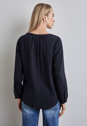 Camisa de manga larga azul marino oscuro hecha de tejido texturizado, con cuello redondo y detalle de fruncido en la parte posterior, combinada con jeans de color azul claro.