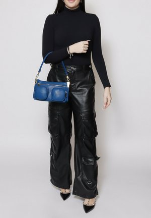 Pantalons larges en cuir noir avec poches, un haut ajusté à manches longues noir, et un petit sac bleu avec deux poches avant et des accents dorés.