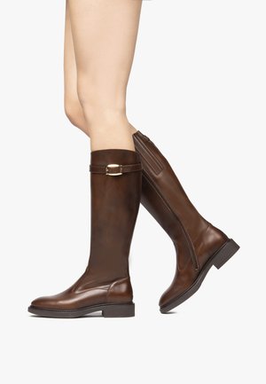 Bottes en cuir marron, montantes jusqu'au genou, avec un bout arrondi, fermeture éclair sur le côté et accent de boucle sur le haut. Texture lisse et semelle robuste.