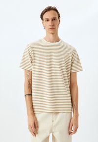 Camiseta de rayas en color crema con franjas horizontales en tono marrón, con cuello redondo y mangas cortas, fabricada en suave tejido de algodón.