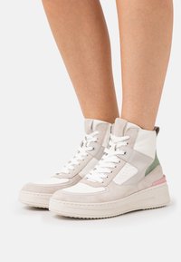 High-top sneakers in beige, white, and pastel green. Made of leather and suede with a textured sole and lace-up design.