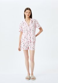 Kortærmet pyjamas sæt i lys pink bomuld med sorte og røde legende mønstre, der inkluderer en skjorte med knap og matchende shorts.