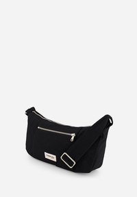 Sac à bandoulière en tissu noir à texture lisse, avec deux poches zippées, une large bandoulière et des accents en métal argenté. Dispose d'un patch avec logo.