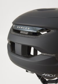 Schwarzer Oakley ARO5 Helm mit mattem Finish, Belüftungsschlitzen, strukturierten Akzenten und einem silbernen Markenlogo auf einem eleganten Design.