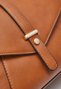 Brązowa skórzana torebka na ramię z zapięciem na klapkę z złotymi okuciami, kontrastującym czarnym przeszyciem i gładką fakturą.