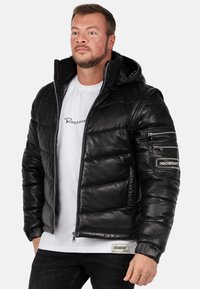 Zwarte leren pufferjack met een capuchon, rits aan de voorkant, gebreide manchetten en een ritszak op de mouw. Kenmerkt logo-accenten.