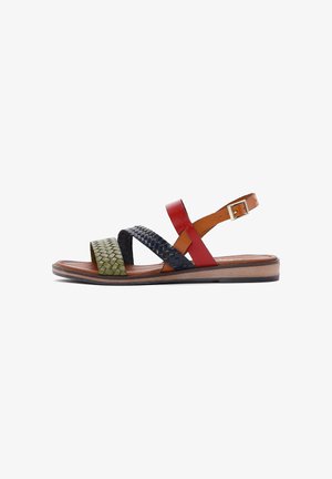 Sandalia plana con correas trenzadas en verde oliva y negro, tira de cuero roja con hebilla en el tobillo y suela marrón con tacón bajo.