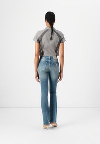 Harmaa lyhythihainen toppi, jossa on valkoiset saumat, yhdistettynä sinisiin levenneisiin farkkuihin. Pehmeä denimi, tummasta vaaleaan harmaaseen sävyliuku, ja hillitty brändäys.