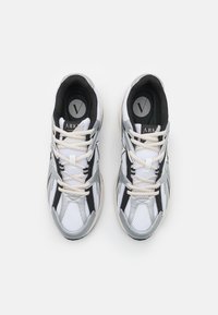 Sneaker sportive con una combinazione di mesh bianco e materiale sintetico argento, dettagli neri e lacci di colore chiaro. Design classico con collo imbottito.