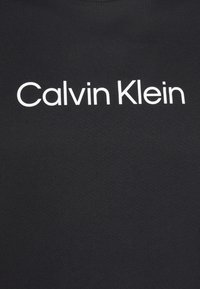 Schwarzes Baumwoll-T-Shirt mit Rundhalsausschnitt, das ein weißes "Calvin Klein"-Logo in einer fetten serifenlosen Schriftart zeigt, aus einem glatten, strukturierten Stoff.