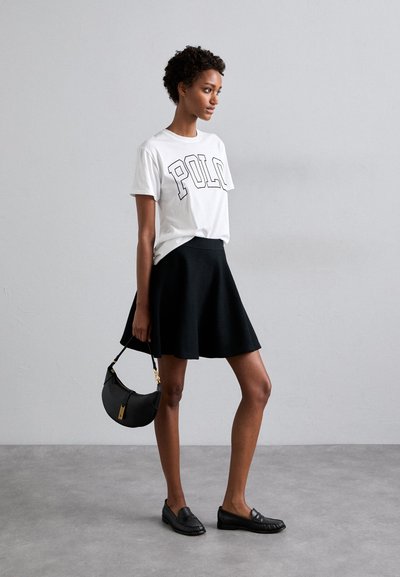 T-shirt blanc avec inscription "POLO", jupe noire évasée, mocassins noirs et un petit sac à main noir avec des accents en métal doré.