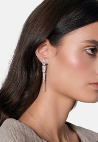 Srebrne kolczyki o kaskadowym wzorze, ozdobione wieloma przezroczystymi kamieniami szlachetnymi, charakteryzujące się teksturowanym wykończeniem i wydłużonym kształtem.