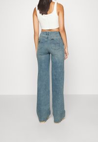 Vaqueros de pierna ancha en denim azul desvaído. Presentan cinco bolsillos, una cintura de altura media y una etiqueta sutil de la marca en el bolsillo trasero.