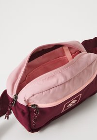 Roza i maroon pojasna torba s dvostrukim zatvaračem, koja ima mekanu teksturu, zaobljeni oblik i unutarnji razdjelnik za organizaciju.