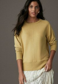 Pull oversized jaune clair avec des poignets et un ourlet côtelés. Texture douce, col rond et une couture nette à l'avant. Associé à une jupe en dentelle.