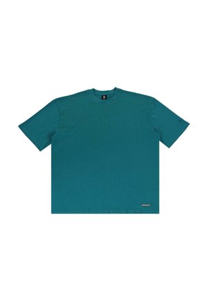 T-shirt en coton teal à manches courtes, col rond et avec un petit patch logo en bas. Texture lisse et coupe décontractée.