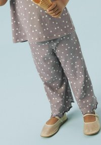 Haut violet clair à pois et pantalons assortis avec un ourlet ondulé. Chaussures beiges avec un bout rond et une bride. Tenant un cornet de glace.