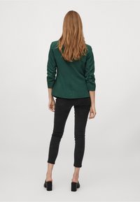 Mörkgrön kavaj med långa ärmar, skräddarsydd passform och slät textur, ihop med svarta slim fit jeans och klackskor med blockklack.