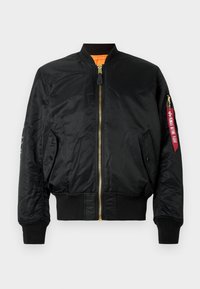 Jachetă bomber neagră, din material lucios, cu fermoar în față, mânici și tiv ribbite. Prezintă o fâă de patch cu litere roșii pe mânecă.