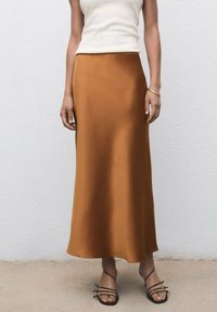 Falda larga de satén marrón con textura lisa y una silueta ligeramente acampanada. Combinada con sandalias negras minimalistas de tiras.