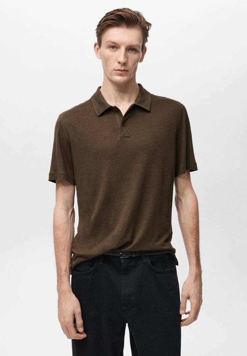 Hnědá polo tričko s krátkým rukávem a límečkem, vyrobené z strukturované tkaniny. Nosené s tmavými kalhotami, které mají minimalistický design a nenápadné švy.