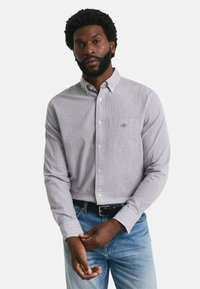Camicia a maniche lunghe a quadri blu, rossa e bianca con colletto button-down e taschino sul petto, abbinata a jeans azzurri chiari e una cintura nera.