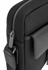 Czarna torba na laptopa z teksturowanym materiałem zewnętrznym, gładkimi skórzanymi akcentami i srebrnym suwakiem z logo.