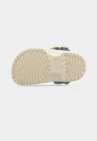 Semelle d'une petite sandale Crocs bleue avec une bande antidérapante beige texturée et des marquages de taille sur un fond blanc.