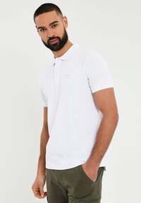 Hvid polo-shirt med en slim fit, korte ærmer og et diskret broderet logo på venstre bryst. Glat bomuldsstof med et klassisk design.