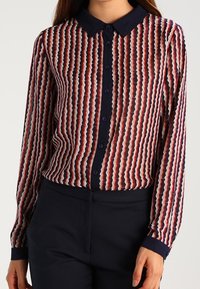Blusa a maniche lunghe realizzata in tessuto trasparente, con motivo a onde in rosso, bianco e blu navy. Design con colletto e chiusura con bottoni, e polsini blu navy.
