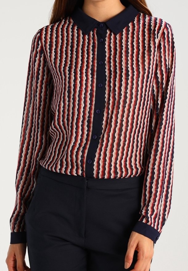 Long-sleeve blouse made of sheer fabric, featuring a wave pattern in red, white, and navy. Collared design with button closure and navy cuffs.