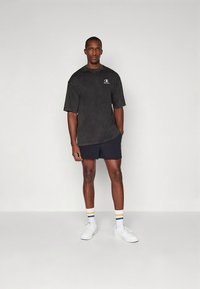 Czarny, oversize'owy t-shirt z krótkim rękawem i logo, zestawiony z granatowymi szortami. Białe trampki i pasiasty skarpetki dopełniają stylizację. Minimalistyczny design.