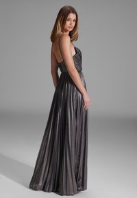 Suknia do ziemi w kolorze ciemnoszarym z metalicznym wykończeniem. Posiada cienkie ramiączka, plisowany krój oraz dopasowaną górę z delikatnym marszczeniem.