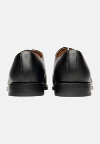 Chaussures en cuir noir avec une finition lisse, un bout rond et un petit talon empilé. Couture minimale et détail de logo au niveau du talon.