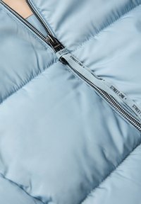 Ljusblå pufferjacka i tyg med kviltade sektioner, med en svart metalldragkedja och en blå dragrem märkt "STREET ONE."