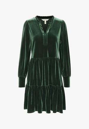 Vestido de terciopelo verde con mangas largas abullonadas, escote en V profundo y volantes fruncidos en la falda. Textura suave con un acabado brillante.