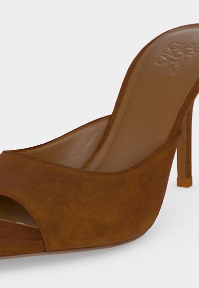 Mule à talon haut en suède marron avec bout ouvert et nom de marque embossé sur la semelle intérieure, montrée en angle sur fond blanc.