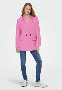 Blazer a doppio petto a righe rosa con lapels a punta, tasche frontali e bottoni neri; indossato su jeans blu e sneakers bianche.