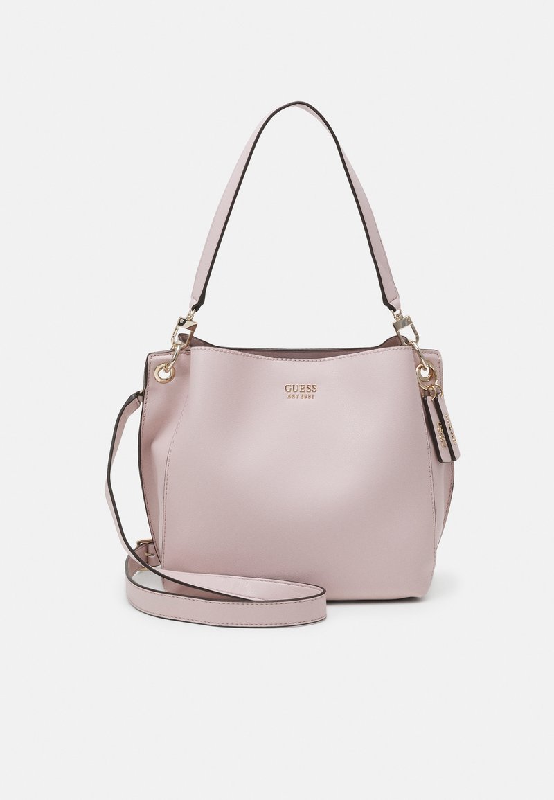 Sac à main Guess en cuir rose pâle avec logo doré, double poignée et bandoulière amovible sur fond uni.