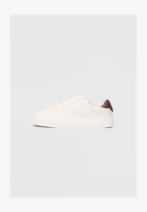 Basket en cuir blanc avec une texture lisse, bout rond, et une accent marron au talon. Présente un laçage à l'avant et une épaisse semelle blanche.
