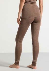 Brune, tettsittende leggings laget av teksturert materiale, med en glatt finish og ankellang design, sett fra en bakre vinkel.