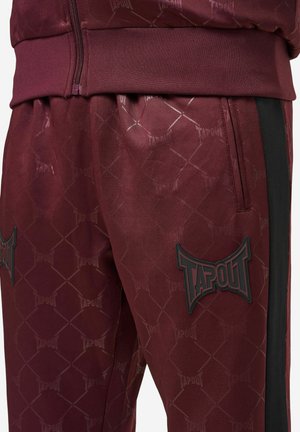 Burgundi värvi spordipüksid, millel on TAPOUT'i bränding, kuusnurkne muster, elastne vöökoht ja külgedel mustad triibud.