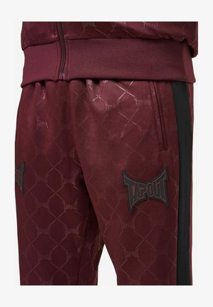 Burgundi värvi spordipüksid, millel on TAPOUT'i bränding, kuusnurkne muster, elastne vöökoht ja külgedel mustad triibud.