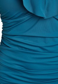 Tealfärgad klädd topp med en volangkrage; gjord av mjukt, töjbart material, som visar fint sömnad och en slät yta.