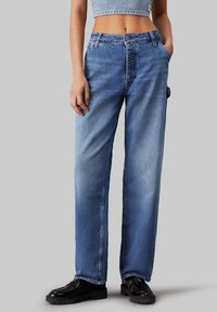 Jeans de mezclilla de pierna ancha en azul claro, con áreas descoloridas, cierre frontal de botón y un bolsillo lateral. Adecuados para un uso casual.