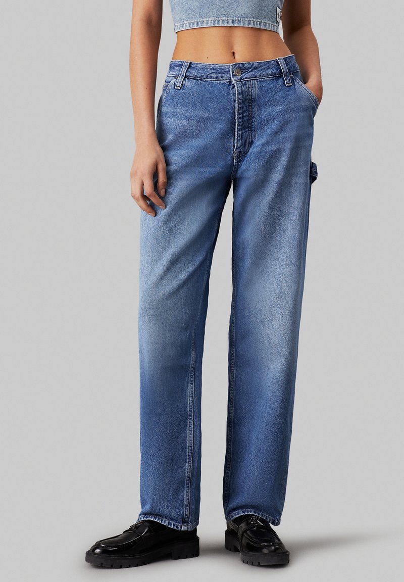 Jeans de mezclilla de pierna ancha en azul claro, con áreas descoloridas, cierre frontal de botón y un bolsillo lateral. Adecuados para un uso casual.