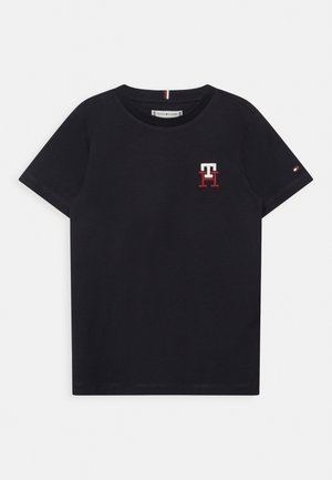 Czarny t-shirt z krótkim rękawem i okrągłym dekoltem, z małym białym i czerwonym logo "TH" po lewej stronie klatki piersiowej oraz małą flagą na lewym rękawie.