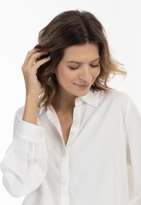 Witte button-up shirt van gladde stof; voorzien van een kraag, knopen aan de voorkant en licht gepofte mouwen met elastische manchetten.